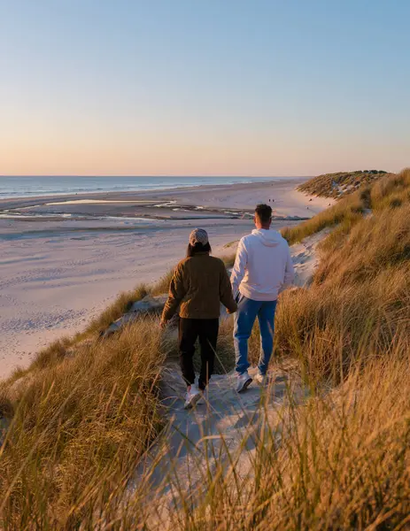 Kumsalın yakınındaki kumlu patikada, güneş sakin suların üzerinde batarken uzun otlarla çevrili birkaç yürüyüş. Altın ışık romantik bir atmosfer yaratır. Vejers Strand Danimarka