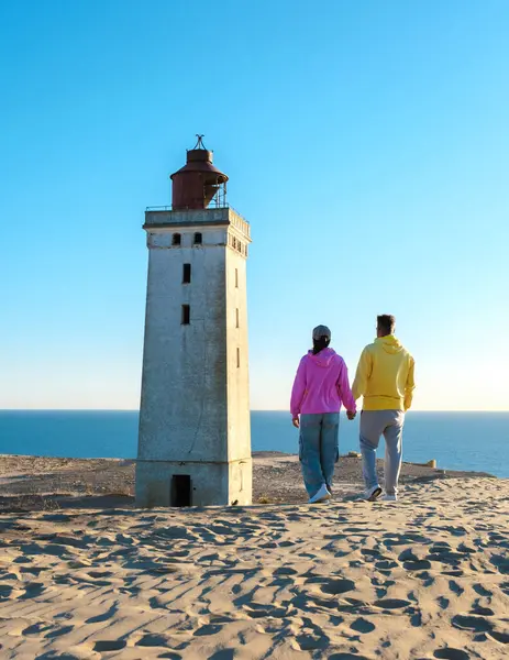 Rubjerg Knude Danimarka 'nın kumlu kumullarında el ele, tarihi deniz fenerine yaklaşıyoruz. Sıcak günbatımı manzaranın üzerine altın bir ışık saçar, 