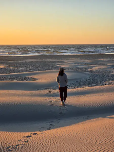 Günbatımında Danimarka 'da bir sahil sahilinin yumuşak kumlarında tek başına gezinen bir figür. Turuncu ve pembe renkli dalgalar yavaşça kıyıya vururken gökyüzünü dolduruyor..
