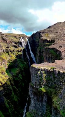 İzlanda 'daki Glymur şelale kanyonunda sarp kayalıklardan akan gizli bir şelalenin nefes kesici güzelliğine tanık olun. Parlak yeşillik engebeli araziyle çelişiyor.