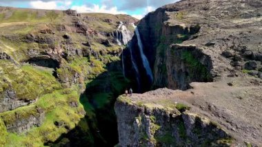 Enfes bir şelalenin parlak manzarası kayalık bir uçurumdan canlı yeşil bir vadiye yuvarlanarak İzlanda 'nın doğal güzelliklerini gözler önüne seriyor. İzlanda 'daki Glymur şelalesinin kıyısında bir çift duruyor.