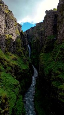 İzlanda 'da bir şelalenin zarifçe kayalıklardan aşağı aktığı, İzlanda' daki Glymur şelalesi kanyonunun nefes kesici güzelliğini deneyimleyin.