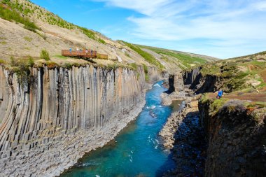 Ziyaretçiler, çarpıcı bazalt sütun kayalıkları arasında canlı mavi suların aktığı Studlagil Kanyonu üzerinde nefes kesen manzaralardan hoşlanıyorlar..