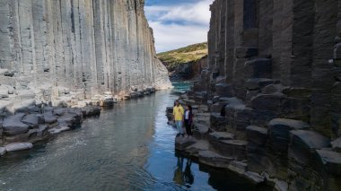 İzlanda 'nın doğal harikalar diyarında parlak bir öğleden sonra iki ziyaretçi bazalt sütunları arasında dururken, bir çift Studlagil Kanyonu' nun şaşırtıcı kaya oluşumlarını ve kristal berrak sularını keşfediyor..