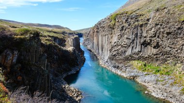 İzlanda 'daki nefes kesici Studlagil Kanyonu' nu keşfedin, eşsiz bazalt sütunları, turkuaz suları ve bereketli yeşillikleri ile, güneşli bir İzlanda gününde açık hava maceraları için idealdir.