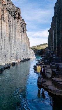Ziyaretçiler, bazalt sütun duvarları ve kristal berrak sularla çevrili Studlagil Kanyonu 'nun çarpıcı jeolojik oluşumlarını keşfediyorlar..