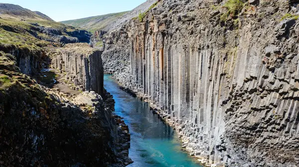 Studlagil Kanyonu 'nun nefes kesici manzarası canlı mavi bir nehrin yanında yükselen bazalt sütunlar. Ziyaretçiler, İzlanda 'nın dramatik manzarası ve eşsiz jeolojik özelliklerinden büyülendiler..