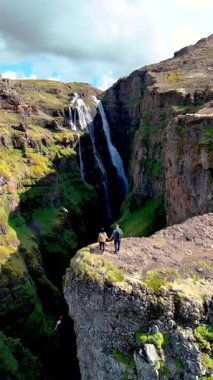 İki maceracı, İzlanda 'nın nefes kesici arazisindeki derin bir kanyona dökülen muhteşem şelaleye hayret ederek kayalık bir uçurum kenarında yürüyor. Glymur şelale kanyonu İzlanda
