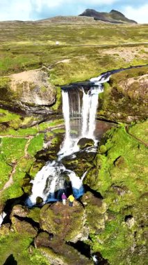 İzlanda 'daki Selvallafoss şelalesinin nefes kesici güzelliğini tecrübe edin. Ziyaretçiler, yemyeşil yemyeşil ve engebeli dağlarla çevrili çağlayan sularda huşu içinde dururlar..