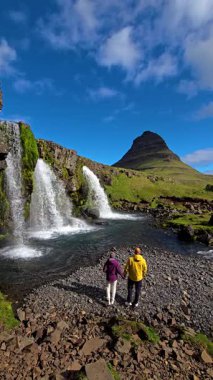 Göz kamaştırıcı şelaleler ve İzlanda 'daki görkemli Kirkjufell dağıyla çevrili, parıldayan bir nehrin kıyısında el ele dolaşırlar.. 