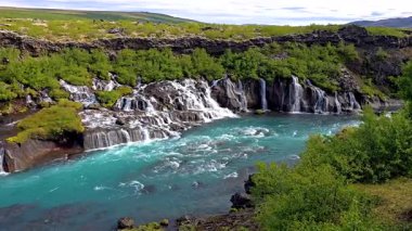 Yeşillikler içinde zarif bir şekilde akan Hraunfossar şelaleleri doğanın nefes kesici bir görüntüsünü sunar. Turkuaz sular, karanlık volkanik kayaların üzerinde çağlayarak büyüleyici bir kontrastlık yaratır..