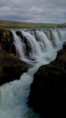 Şelaleler engebeli kaya oluşumlarından akarken nefes kesici Kolugljufur Kanyonunu keşfedin. Alacakaranlık gökyüzü bu büyüleyici İzlanda manzarasına huzur dolu bir ortam yaratıyor..