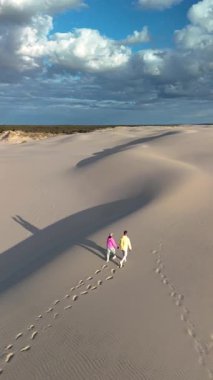 Danimarka 'nın Rabjerg Mile Jutland kentinin geniş kum tepelerinde altın saat boyunca iki kişi el ele yürür. Yumuşak gölgeler ve ılık ışık huzur verir.