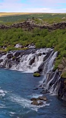 Dramatik şelale, yemyeşil ve berrak mavi sularla çevrili engebeli uçurumların üzerinden nazikçe akıyor. Bu sakin doğal ortam İzlanda 'nın çarpıcı güzelliğini ve çeşitli coğrafyasını sergiliyor..