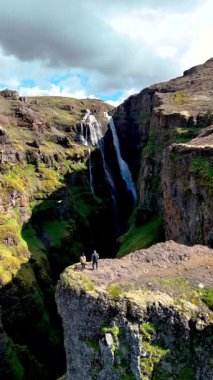 İki maceraperest İzlanda 'daki büyüleyici Glymur şelalesi kanyonunda, İzlanda' da dramatik uçurumlar ve yemyeşil alanlarla çevrili. Parlak ufuk doğal güzelliği sergiliyor.
