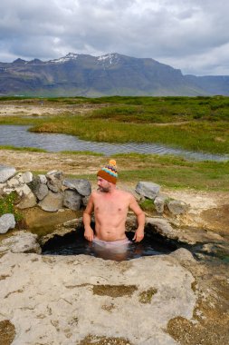Landbrotalaug Kaplıcaları 'nda, İzlanda' nın göz kamaştırıcı manzarasının tadını çıkarıyorum. Doğa güzelliği arka planda belirdikçe, hafif buhar yükselir. İzlanda 'da sıcak bir jeotermal havuzda erkekler