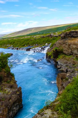 Barnafoss ve Hraunfossar 'daki engebeli kayaların üzerinde kristal gibi berrak sular taşar. İzlanda 'daki bu nefes kesici manzara, canlı yeşillikler ve açık mavi gökyüzünün ortasındaki güzelliği gözler önüne seriyor..