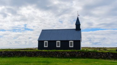 İzlanda 'nın geniş alanlarında, keskin çan kulesiyle geleneksel İskandinav mimarisini sergileyen antika siyah bir kilise. Serin bulutlar Budakirkja üzerinde canlı bir zemin oluşturur.