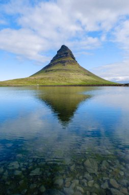 Benzersiz şekliyle karakterize edilen Kirkjufell Dağı 'nın manzarası İzlanda' daki sakin bir gölün üzerinde görkemli bir şekilde yükseliyor.