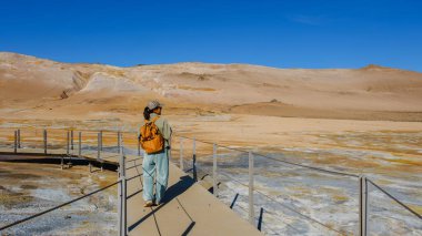 Asyalı kadın gezgin, dramatik ve renkli arazilerle çevrili İzlanda jeotermal bölgesinde insan yapımı yollar boyunca yürüyor..