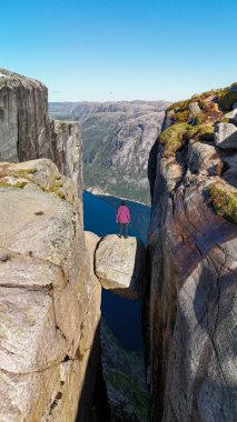 Ünlü Kjeragbolten kayasının tepesinde duran bir gezgin, fjord manzaralarına ve dik kayalıklara bakıyor. Bu macera noktası Norveç, Kjeragbolten Lysefjord, Norveç 'in saf güzelliğini yansıtıyor.