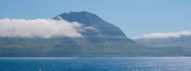Sakin denizin üzerinde yükselen Faroe Adaları 'ndaki çarpıcı bir dağ kısmen bulutlarla örtülüdür. Bereketli yeşil arazi ve canlı sular doğa severler için mükemmel bir ortam yaratır..