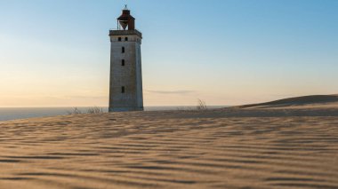 Rubjerg Knude Deniz Feneri, Kuzey Denizi 'nin üzerinde güneş batarken altın kum tepelerinin arasında görkemli bir şekilde duruyor.