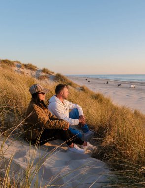 Kumlu bir kumulda birlikte dinlenen bir çift, sakin Danimarka kıyı şeridinde güneşin sıcacık parıltısına hayran. Vejers Strand Sahili Danimarka