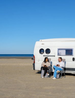 İki gezgin Lakolk Strand, Romo, Danimarka kıyılarında huzurlu bir anın tadını çıkarıyor, içkilerini yudumluyor ve kıyı manzarasının tadını çıkarıyorlar. Karavan bu güzel kumsalda rahat bir dinlenme yeri sağlıyor..