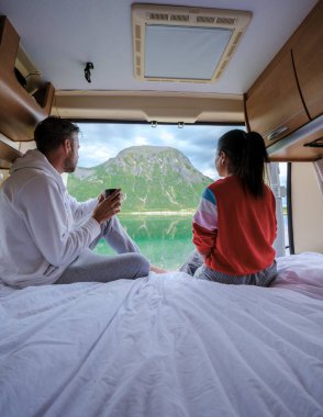 Bir çift, Norveç 'te nefes kesen fiyort manzarasına hayran kalarak karavanlarında sakin bir sabahın tadını çıkarıyor. Bu canlı manzara, Lofoten 'daki barışçıl inzivalarını tamamlıyor.