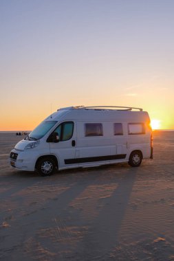 Gün batımında sakin bir Danimarka plajına park etmiş rahat bir karavan. Batan güneşin ılık renkleri kuma yansıyor, Lakolk Strand, Romo Danimarka