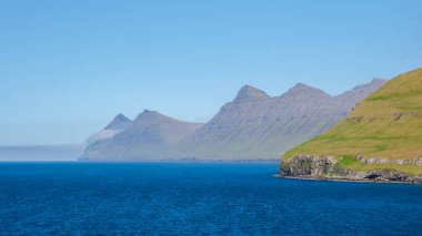 Faroe Adaları 'ndaki Atlantik Okyanusu' nun derin mavi sularından çarpıcı uçurumlar yükselir. Yeşillik yemyeşil yamaçları örtüyor ve gökyüzüne karşı nefes kesici bir kontrastlık oluşturuyor..