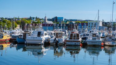 Torshavn, Faroe Adaları 22 Mayıs 2025, sakin sulara yansıyan renkli binalar sergileniyor. Balıkçı tekneleri rıhtımda yüzüyor, Faroe Adaları 'ndaki açık mavi gökyüzünün altında pitoresk bir manzara yaratıyor..