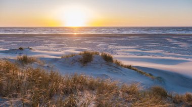 Altın renkler, güneş Danimarka kıyı şeridinde batarken kumulları aydınlatarak doğanın denizle huzur içinde buluştuğu huzurlu bir atmosfer yaratıyor. Vejers Strand, Danimarka