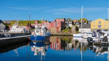 Torshavn, Faroe Adaları, 22 Mayıs 2025, renkli evler kıyı boyunca uzanırken balıkçı tekneleri sakin sularda sallanıyor. Parlak mavi gökyüzü bu güzel manzaranın huzur dolu güzelliğine katkı yapıyor..