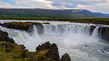 Güçlü şelaleler, yemyeşil ve dramatik manzaralarla çevrili Godafoss İzlanda 'daki kayalık kayalıklara hücum ediyor. Sahne İzlanda 'nın nefes kesen doğal güzelliklerini yansıtıyor..