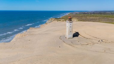 Rubjerg Knude North Jutland Danimarka 'nın kumlu sahillerinde ikonik bir deniz feneri barındıran çarpıcı bir kıyı manzarası. Turkuaz dalgalar kıyıya çarpıyor.