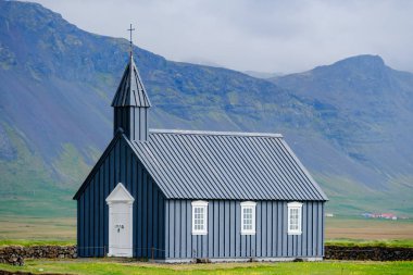Budakirkja siyah kilisesi, İzlanda 'nın nefes kesici dağları arasında duruyor ve geleneksel mimariyi gözler önüne seriyor. Yumuşak bulutlar yukarıda süzülür ve bu uzak yerin sakin atmosferine eklenir..