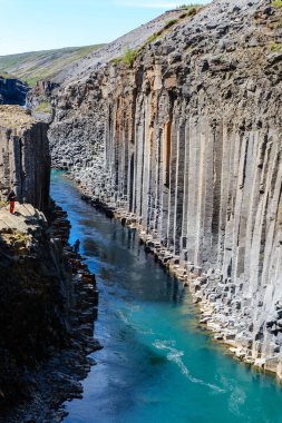 Ziyaretçiler, İzlanda 'da hayranlık uyandıran bir doğa harikası olan Studlagil Kanyonu' nun yüksek bazalt sütunlarına ve canlı mavi sularına hayret ediyorlar..