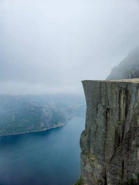 Sisli hava Norveç 'in dramatik uçurumlarını kaplayarak büyüleyici bir atmosfer yaratır. Aşağıdaki sakin sular görkemli manzarayı yansıtıyor, kaşifleri doğa harikalarını takdir etmeye davet ediyor..