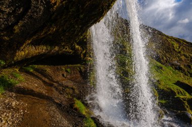 Selvallafoss şelalesi dalgalı yeşil yosun ve İzlanda 'nın kayalık arazisiyle çevrili engebeli uçurumların üzerinden akar.