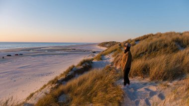 Danimarka 'da sakin bir sahil, günbatımının güzelliğini yakalar. Yalnız bir figür kumların üzerinde duruyor, altın kumlara ve sakin denize hayran, dinlenmek için mükemmel huzurlu bir atmosfer yaratıyor..