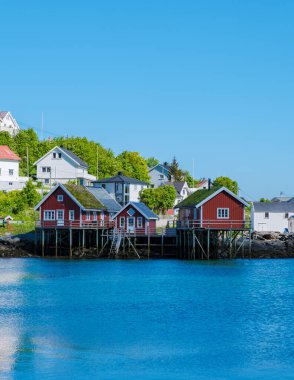 Renkli ahşap kulübeler Norveç 'teki rıhtım boyunca uzanır, yemyeşil bir zemin ve parlak mavi bir denize karşı kurulur. Huzurlu atmosfer rahatlama ve keşfi davet eder. Lofoten Reine