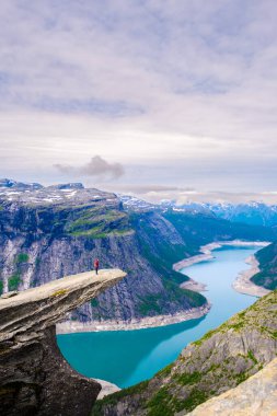 Yalnız bir yürüyüşçü dramatik bir uçurumun kenarında duruyor, Norveç 'in Trolltunga kentindeki görkemli dağlarla çevrili bir fiyordun turkuaz sularına bakıyor. Atmosfer sakin ve nefes kesici..