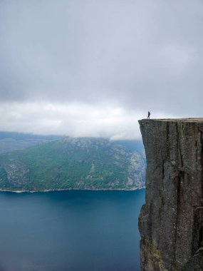 Yalnız bir figür dramatik bir uçurumun kenarında duruyor, sakin sulara bakan ve bereketli dağlara bakan Preikestolen Cliff Norveç 'in sakin atmosferi bu uzak yerin güzelliğini yakalıyor..