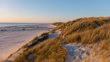 Gün batımında Danimarka 'nın Vejers Strand sahilinde sakin bir sahile uzanan yumuşak kum tepelerinin nefes kesici manzarası..