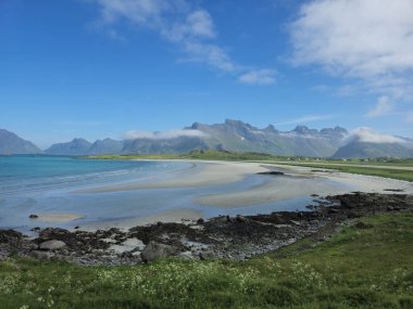 Sahil güzelliği, arka planda görkemli dağlar bulunan Norveç kıyıları boyunca uzanır. Sakin sular, huzurlu bir keşif ya da rahatlama günü için mükemmel bir gökyüzünü yansıtır..