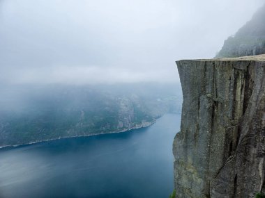 Engebeli bir uçurumun kenarından nefes kesici bir manzara sisli bulutlar manzaralı sularda yuvarlanıyor. Önceki Uçurum Norveç 
