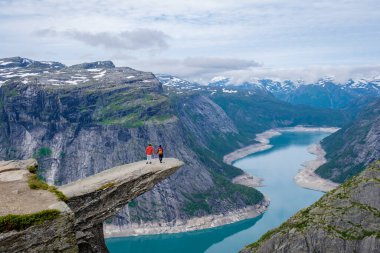 İki yürüyüşçü ikonik Trolltunga uçurumunun kenarında duruyor, Norveç 'teki muhteşem fiyorda yukarıdan bakıyor.