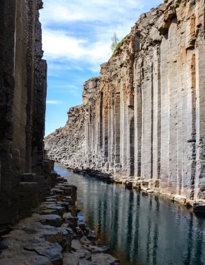 Studlagil Kanyonu 'nun eşsiz güzelliğini deneyimleyin. İzlanda' daki sakin suların yanında çarpıcı bazalt sütunlar görkemli bir şekilde yükseliyor.